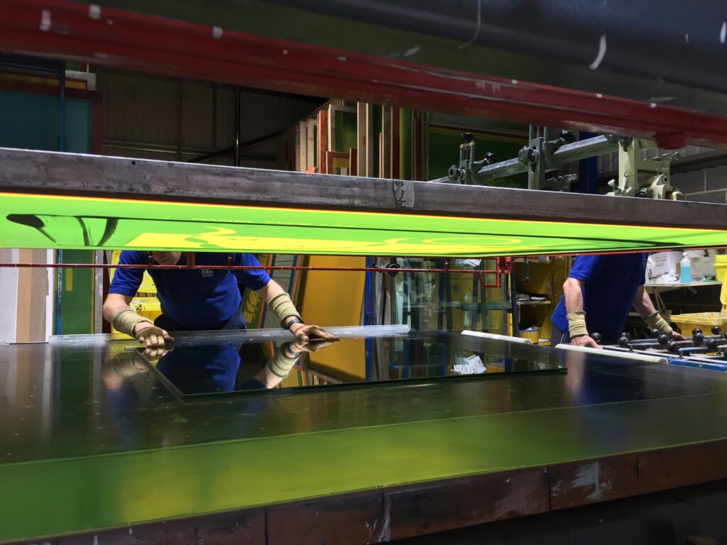 Image shows two men working on printed glass at Kite Glass Weybridge to illustrate the work of the security glass manufacturers